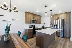 Kitchen featuring stainless steel appliances, a center island, light wood-type flooring, and light stone countertops