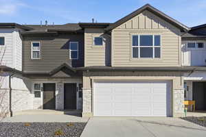 View of front of property with stone siding, an attached garage, board and batten siding, concrete driveway, and a shingled roof