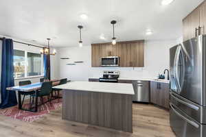 Kitchen with stainless steel appliances, a kitchen island, light wood-type flooring, decorative backsplash, and modern cabinets