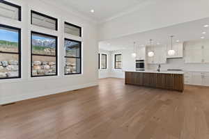 Kitchen with dual tone cabinets, open floor plan, light countertops, light wood-type flooring, and an island with sink