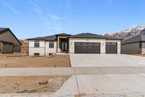 Prairie-style house with an attached garage, concrete driveway, stone siding, a mountain view, and a shingled roof