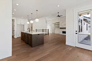 Kitchen with dual tone cabinetry, hanging light fixtures, open floor plan, an island with sink, and dark wood finished floors