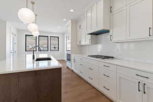 Kitchen featuring light wood-style floors, hanging light fixtures, white cabinets, and light stone counters