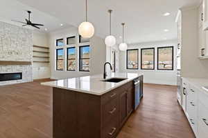 Dual tone kitchen featuring two tone color scheme, a stone fireplace, open floor plan, decorative light fixtures, and light wood-style floors
