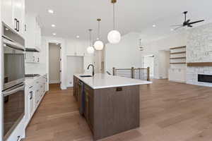 Kitchen with two tone cabinets, stainless steel appliances, open floor plan, light wood-style flooring, and a center island with sink