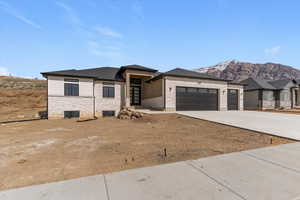 Prairie-style home featuring stone siding, a garage, driveway, a mountain view, and roof with shingles