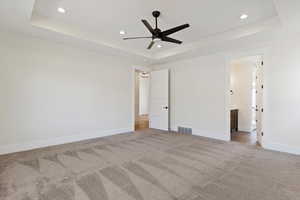 Unfurnished bedroom with a raised ceiling, light colored carpet, ceiling fan, recessed lighting, and ensuite bath