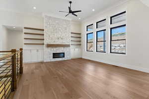 Unfurnished living room with a stone fireplace, ceiling fan, light wood finished floors, ornamental molding, and recessed lighting