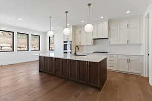 Kitchen with two tone color scheme, a kitchen island with sink, light wood-style floors, decorative light fixtures, and light stone counters