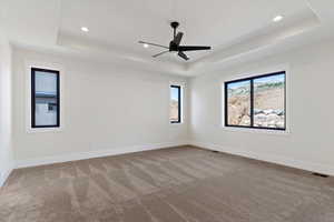 Empty room with light carpet, a raised ceiling, ceiling fan, and recessed lighting