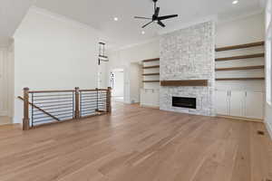 Unfurnished living room with a stone fireplace, light wood finished floors, ceiling fan, ornamental molding, and recessed lighting