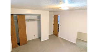 Unfurnished bedroom with light colored carpet, a closet, and a textured ceiling