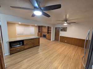 Kitchen featuring stainless steel appliances, granite countertops, a wainscoted wall, ceiling fans, a granite kitchen island, and a fireplace