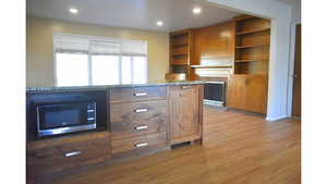 Kitchen with light wood-type flooring, light stone counters, open shelves, recessed lighting,  wood finish cabinetry, and wood-burning fireplace.