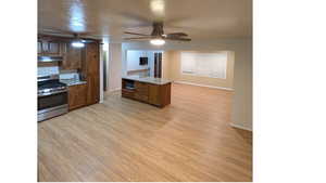 Kitchen looking into the living area with stainless steel appliances, light wood-style floors, a ceiling fan, wood finish shaker cabinets and granite counters and island.