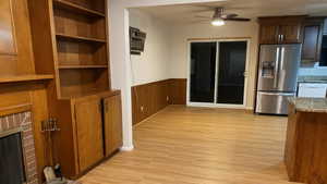 Unfurnished dining area featuring a wainscoted wall, light wood-style flooring, ceiling fan, wood walls, and a fireplace