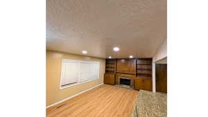 Unfurnished living room featuring a textured ceiling, recessed lighting, a brick fireplace, and light wood-type flooring