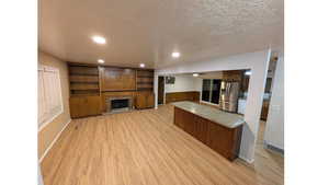 Unfurnished living room featuring light wood-type flooring, a textured ceiling, a fireplace with built in shelves and cabinets, , recessed lighting.