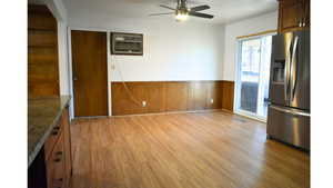 Unfurnished dining area featuring wood walls, wainscoting, dark wood-style flooring, and ceiling fan