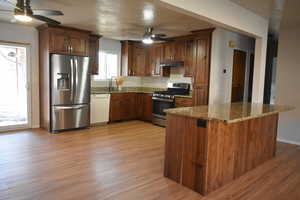 Kitchen with stainless steel appliances and farmhouse sink, granite counters, island, shaker cabinets,  ceiling fans, and light wood-style floors.