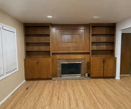 Unfurnished living room featuring light wood-style flooring, a fireplace, built in shelves and cabinets, and recessed lighting