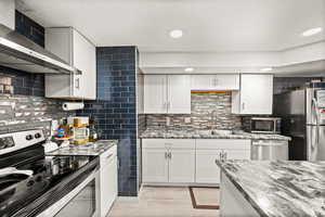 Kitchen featuring stainless steel appliances, dark stone countertops, white cabinets, tasteful backsplash, and recessed lighting