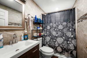 Bathroom featuring tile walls, vanity, curtained shower, and decorative backsplash