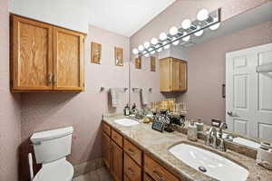 Full bathroom with double vanity, wallpapered walls, and light tile patterned floors