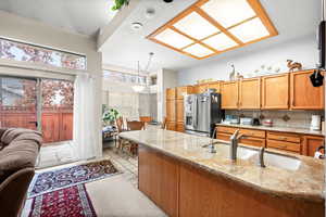 Kitchen featuring stainless steel fridge with ice dispenser, light stone countertops, hanging light fixtures, wood finish cabinets, and decorative backsplash