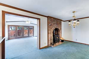 Unfurnished living room with ornamental molding, carpet flooring, a wood stove, ceiling fan, and a chandelier