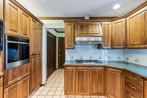 Kitchen featuring stainless steel appliances, wood finish cabinets, a textured ceiling, backsplash, and light tile patterned floors