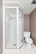 Bathroom featuring wallpapered walls, a shower stall, a textured ceiling, and light tile patterned floors