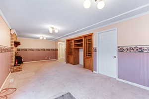 Basement with wainscoting, a wood stove, light carpet, a textured ceiling, and crown molding