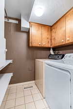 Laundry room featuring a textured ceiling, independent washer and dryer, cabinet space, and light tile patterned flooring
