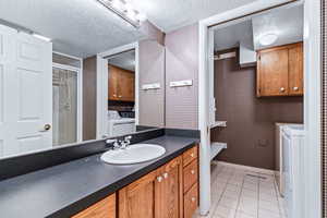 Full bathroom with vanity, a textured ceiling, light tile patterned flooring, independent washer and dryer, and a shower stall