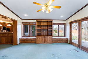 Unfurnished living room with lofted ceiling, light colored carpet, a ceiling fan, ornamental molding, and plenty of natural light