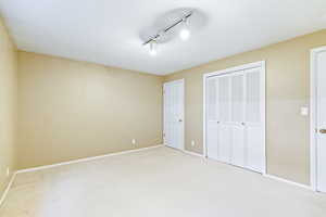 Unfurnished bedroom featuring rail lighting, light colored carpet, a closet, and a textured ceiling