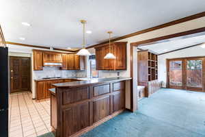 Kitchen featuring crown molding, wood finish cabinets, a peninsula, tasteful backsplash, and pendant lighting