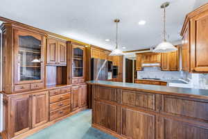 Kitchen featuring wood finish cabinets, a peninsula, pendant lighting, light colored carpet, and a textured ceiling