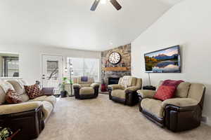 Living room featuring vaulted ceiling, a ceiling fan, a fireplace, and carpet flooring