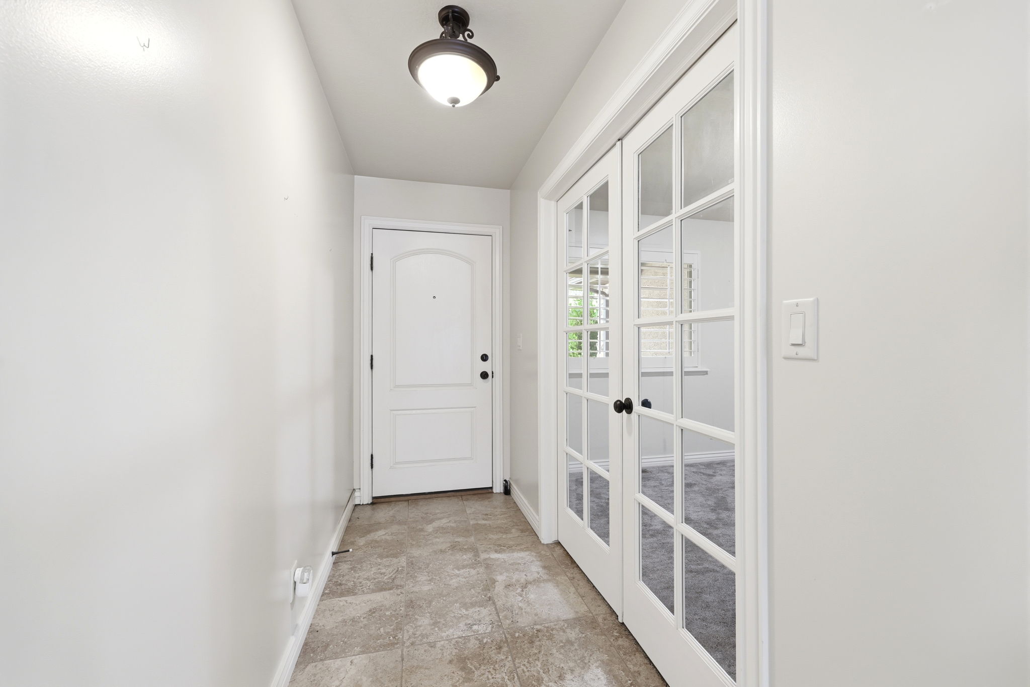 Entryway featuring light-toned tile flooring, a paneled entry door, and a built-in ceiling light fixture