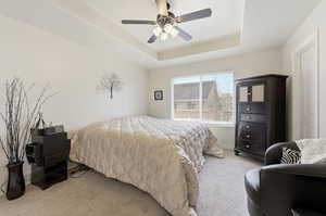 Bedroom featuring light colored carpet, a tray ceiling, and ceiling fan