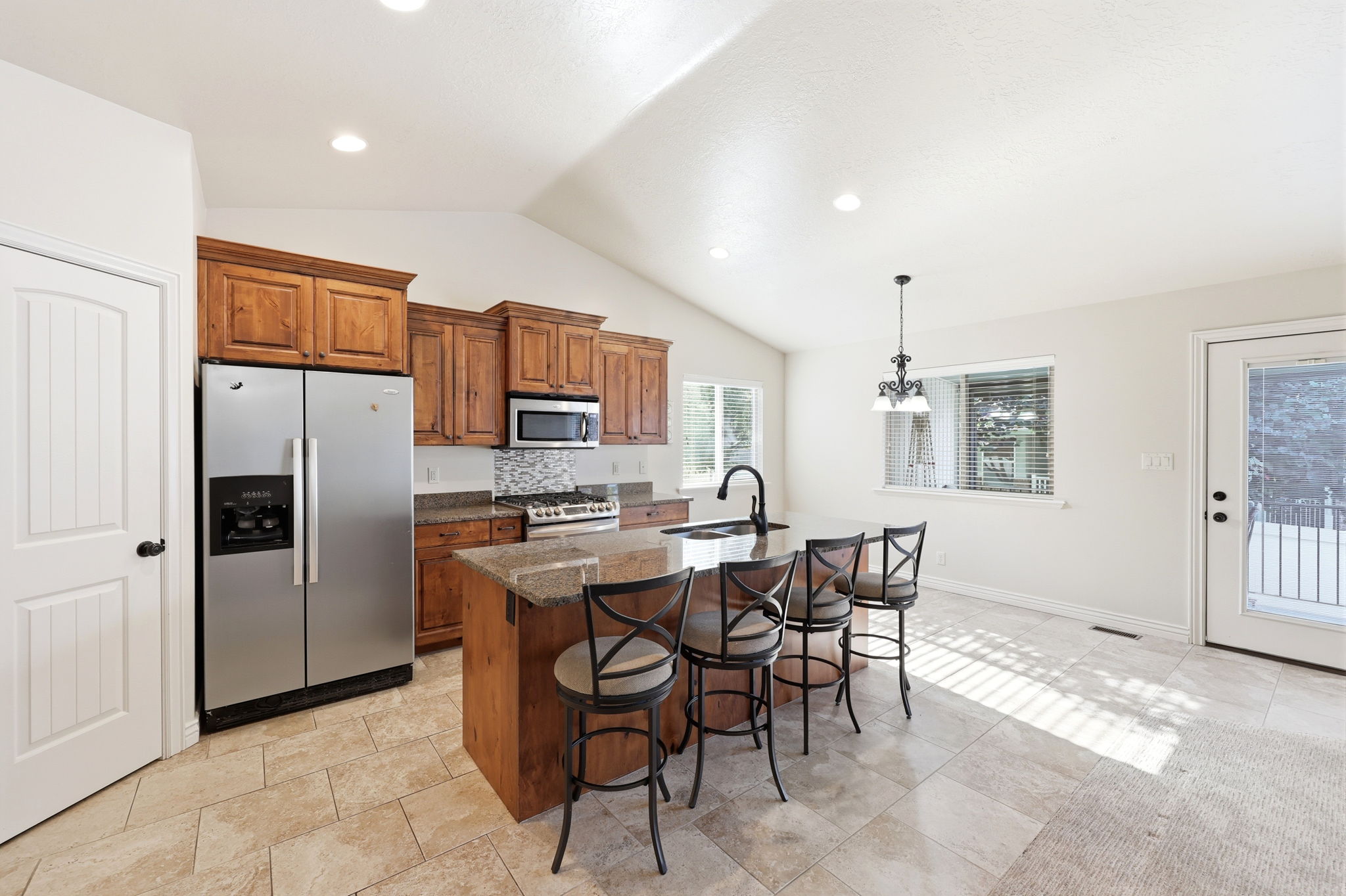Open-concept kitchen featuring vaulted ceilings, recessed lighting, wood-finish cabinetry, a central island with bar seating, and tile flooring