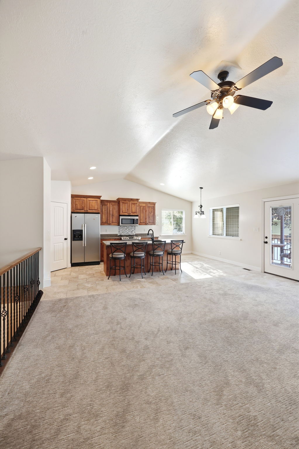 Spacious open-concept living area featuring vaulted ceilings, ceiling fan with light, and light-toned carpeting