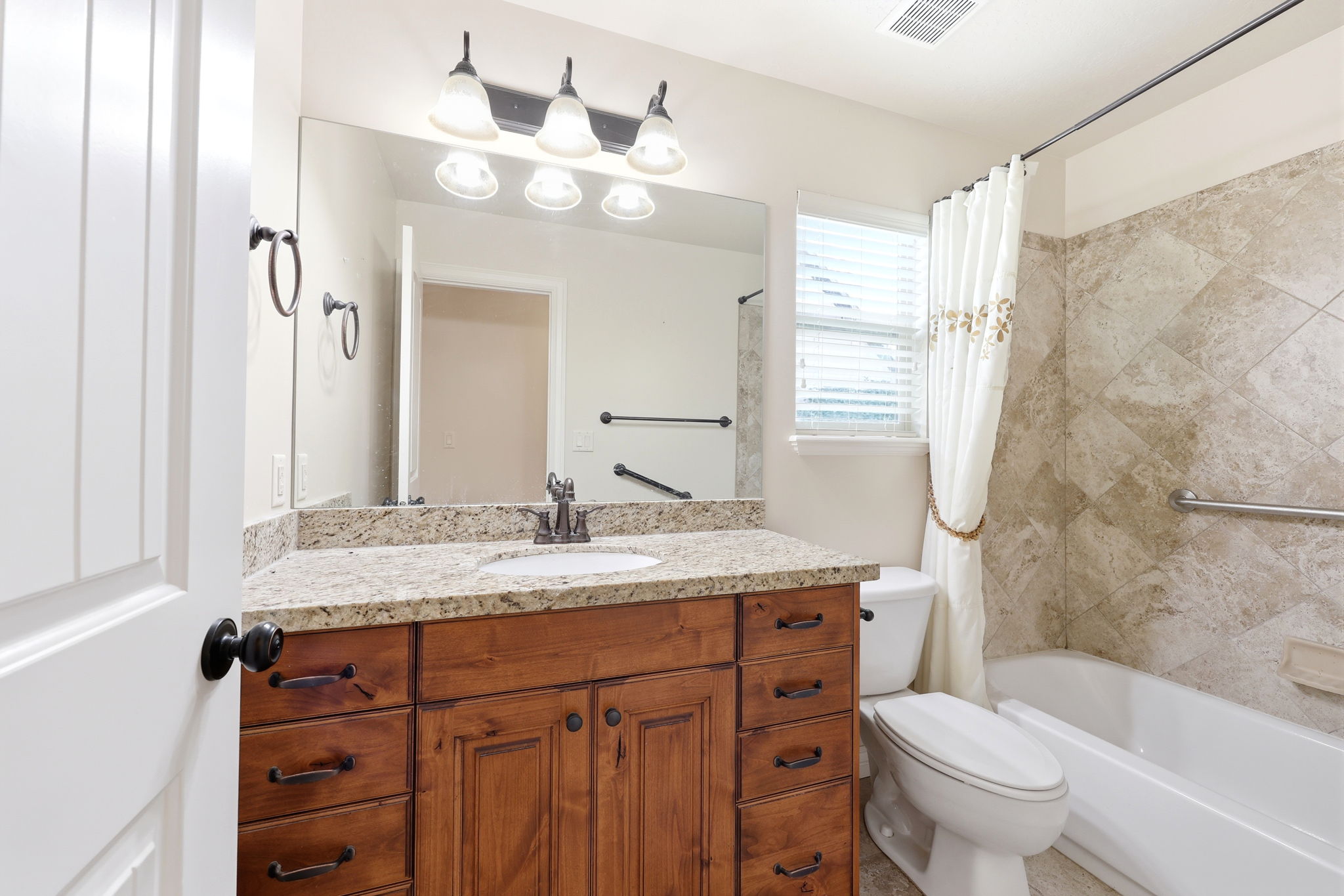 Bathroom featuring a wood-finish vanity with granite-style countertop, integrated sink, and an expansive mirror