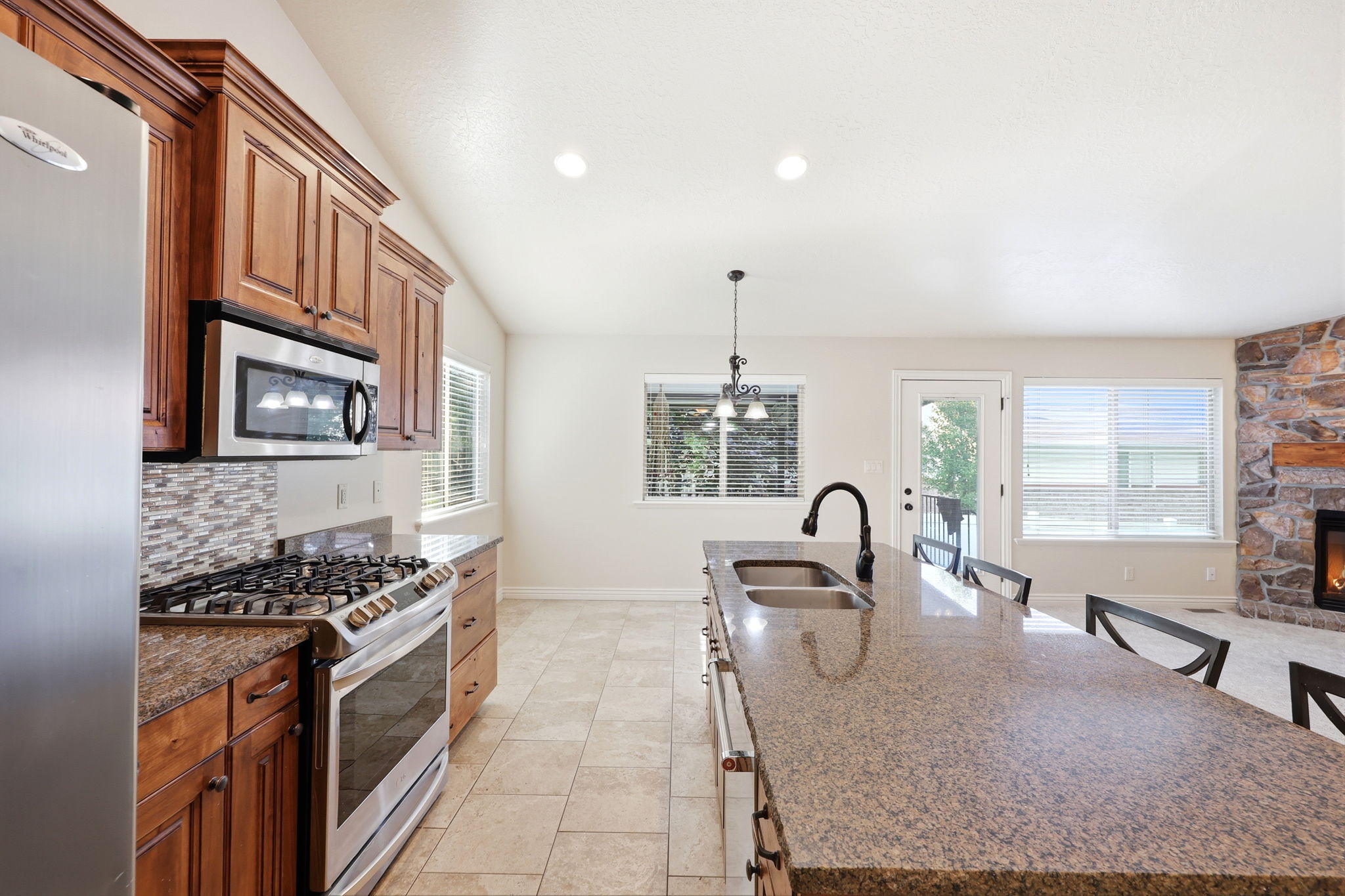 Spacious kitchen featuring an expansive island with a double basin sink, stainless steel appliances, wood cabinetry, and tile flooring