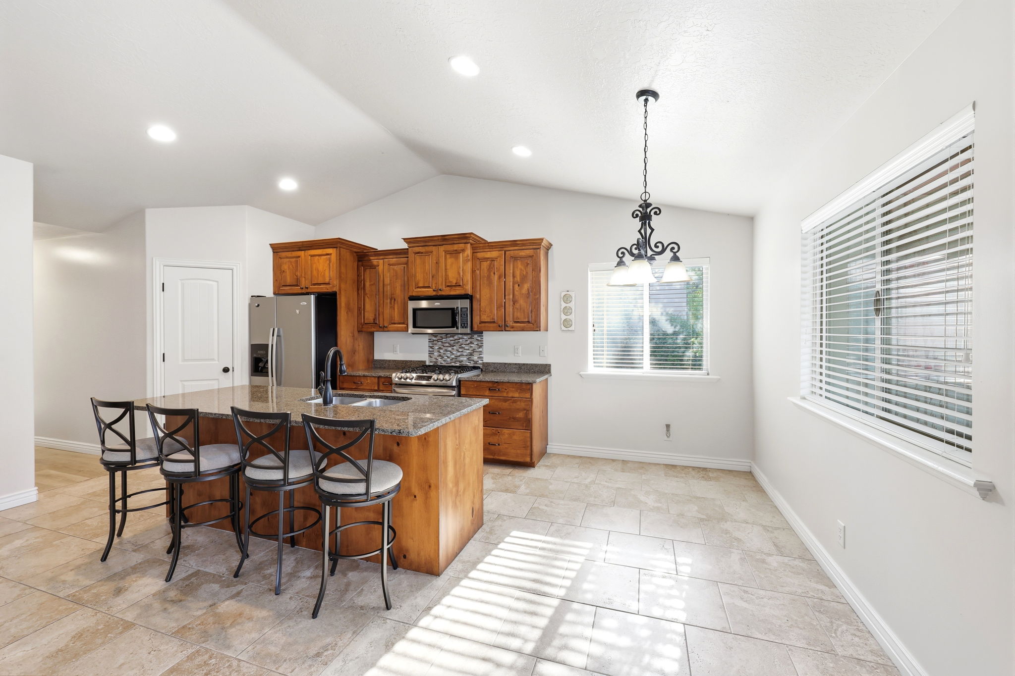 Kitchen featuring a large island with counter seating, wood cabinetry, stainless steel appliances, a tile backsplash, and light tile flooring