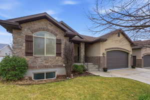 View of front facade with stone siding, an attached garage, a front lawn, concrete driveway, and stucco siding
