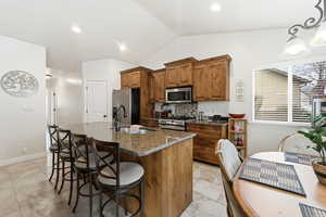 Kitchen with wood finish cabinetry, dark stone counters, a breakfast bar area, a kitchen island with sink, and stainless steel appliances