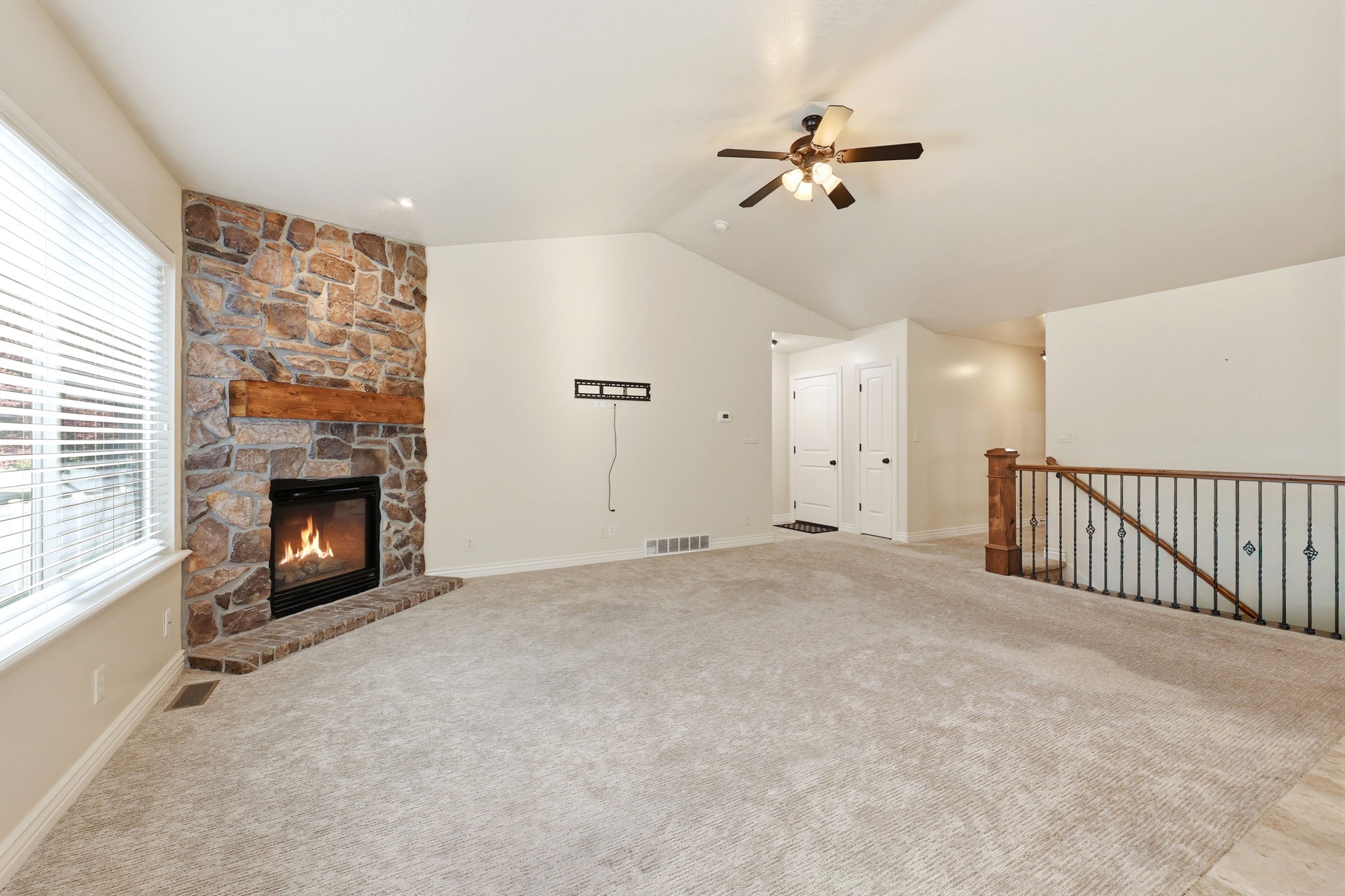 Spacious living area featuring a stone fireplace with a wood-finish mantel, vaulted ceilings, and light-toned carpeting